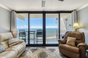 Una sala de estar con un sofá, un sillón y vista al océano a través de una puerta corrediza de vidrio.