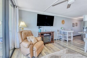 A living room with a leather sofa, a flat-screen TV, a dining table with chairs, and a kitchen area with a refrigerator. - Royal Garden Resort 812 - Two Bedroom, Two Bath Oceanfront Condo (Garden City Beach)