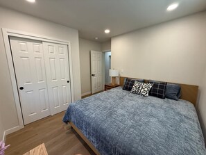 A bedroom with a bed, a nightstand, a lamp, and a door. - Modern 3-Bedroom Home with Garage, Smart TVs, and Laundry Facilities. (Merced)
