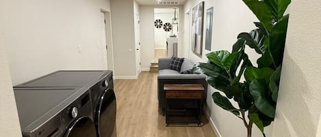 A laundry area with a washing machine and dryer, a small seating area with a bench, and a potted plant.