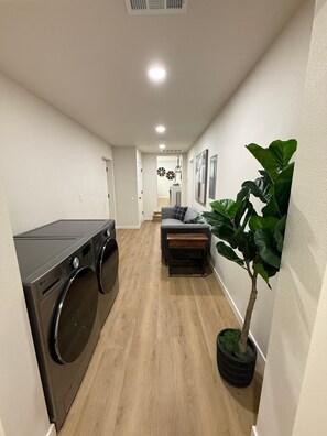 Een wasruimte met een wasmachine en droger, een klein zithoekje met een bankje, en een kamerplant.