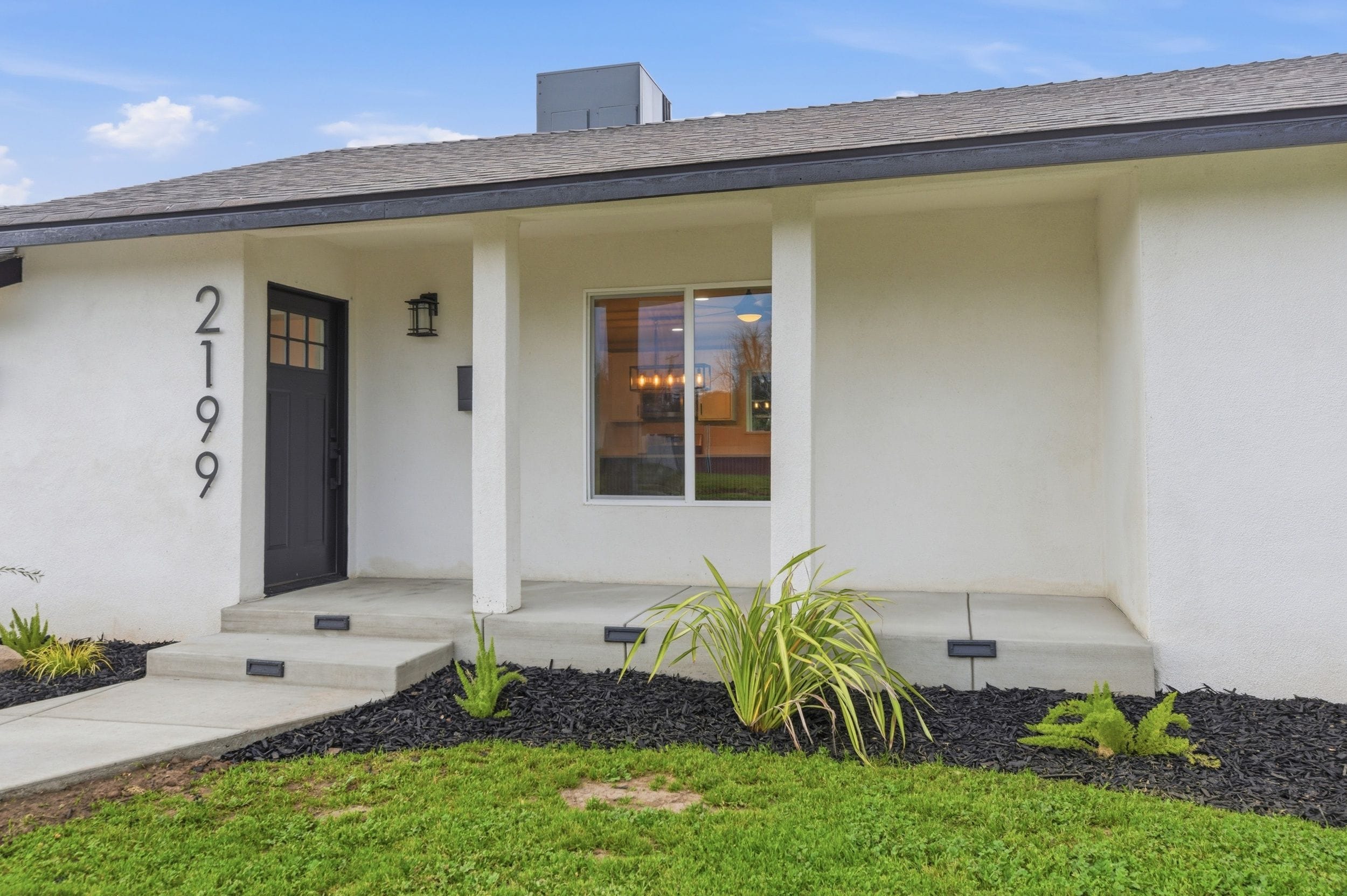 A modern two-story house with a black front door, a small porch, and a number '2199' on the wall.