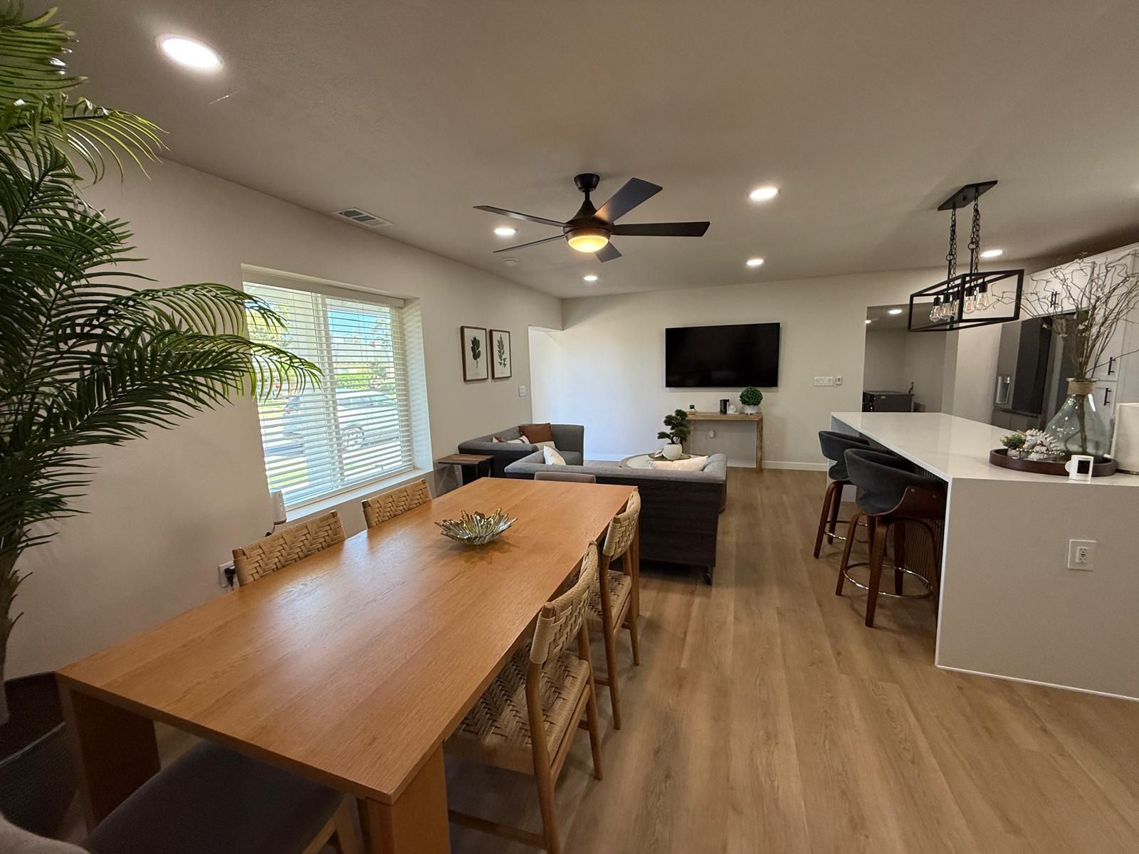 A modern kitchen with a central island, a dining area with a wooden table and chairs, and a ceiling fan.