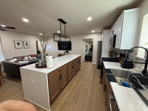 A modern kitchen with a central island, wooden cabinets, and a built-in oven. - Modern 3-Bedroom Home with Garage, Smart TVs, and Laundry Facilities. (Merced)