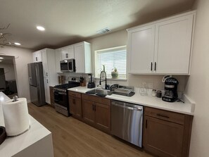 A modern kitchen with white cabinets, stainless steel appliances, and a window with blinds.