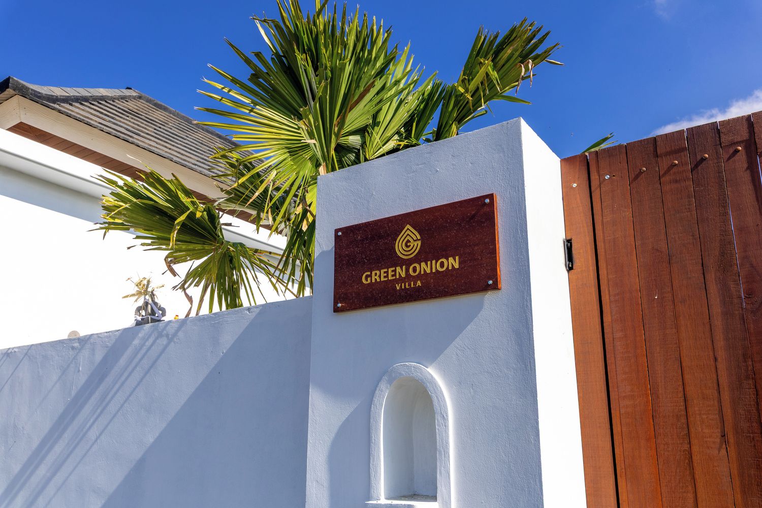 A sign for 'GREEN ONION VILLA' with a logo, a white wall, and a wooden fence.