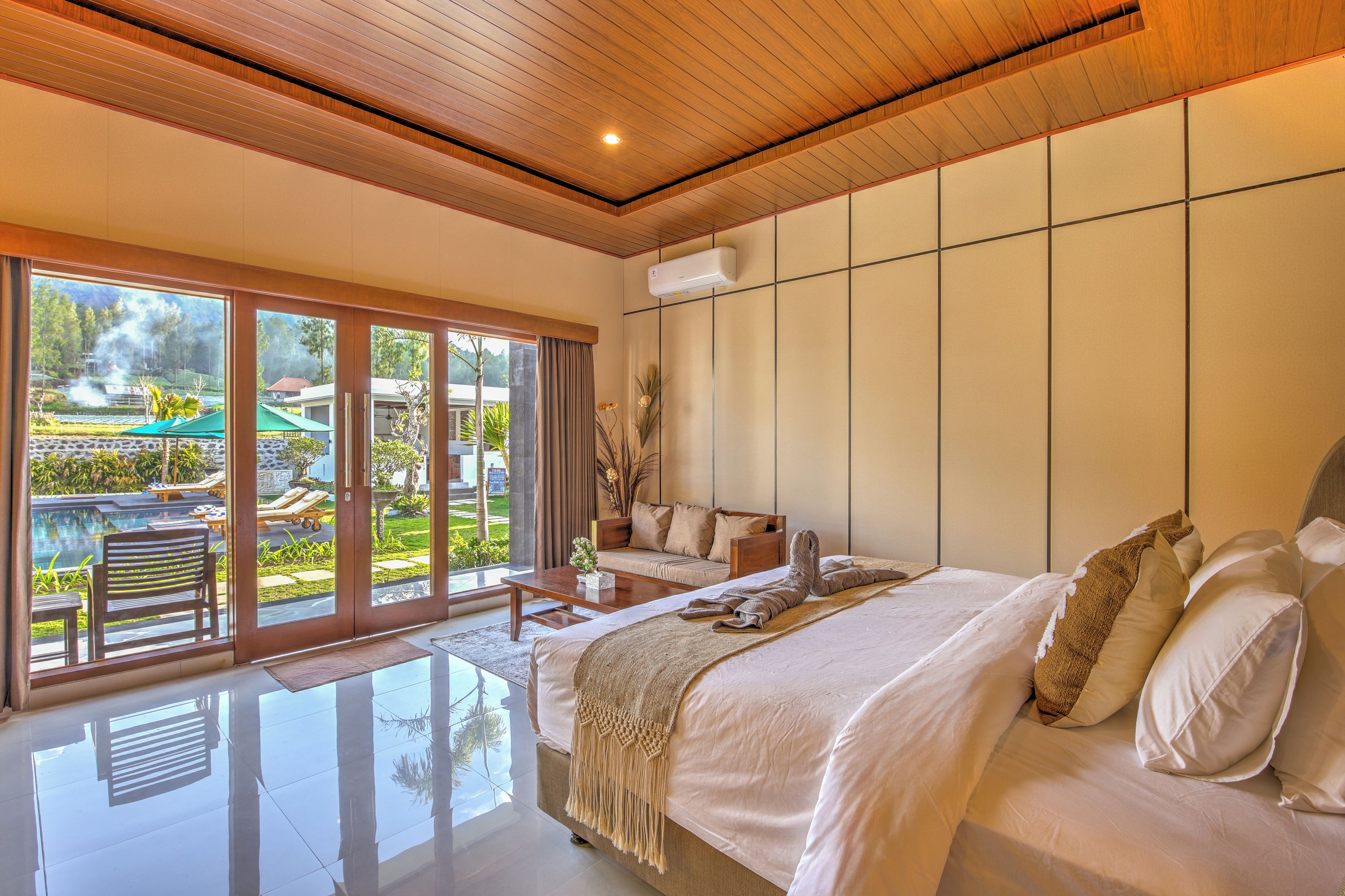 Habitación de hotel moderna con una cama grande, zona de estar y vistas a una piscina y jardín.