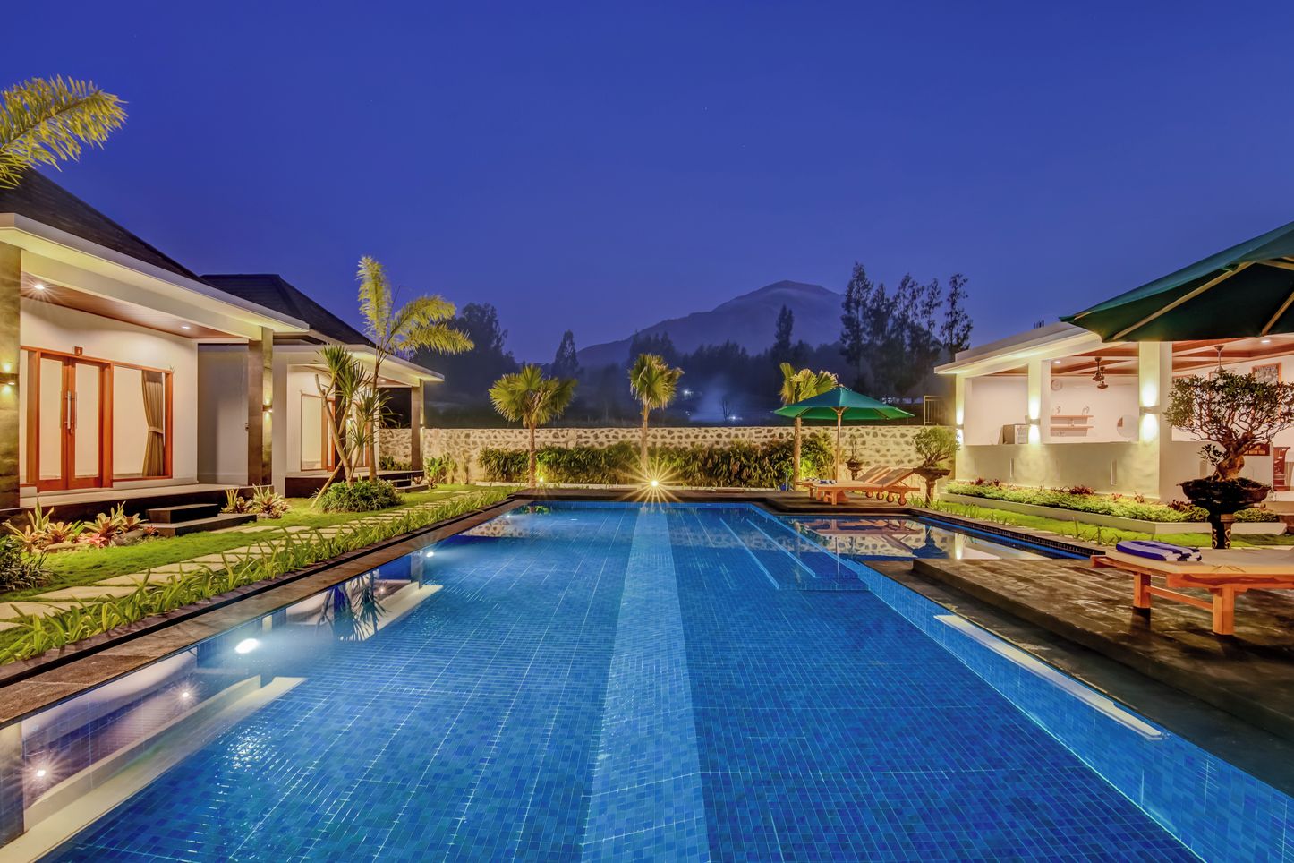 A swimming pool with a view of mountains in the background, surrounded by well-maintained gardens and outdoor seating areas.