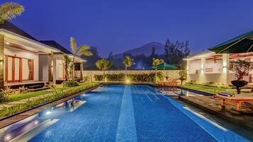 A swimming pool with a view of mountains in the background, surrounded by well-maintained gardens and outdoor seating areas.