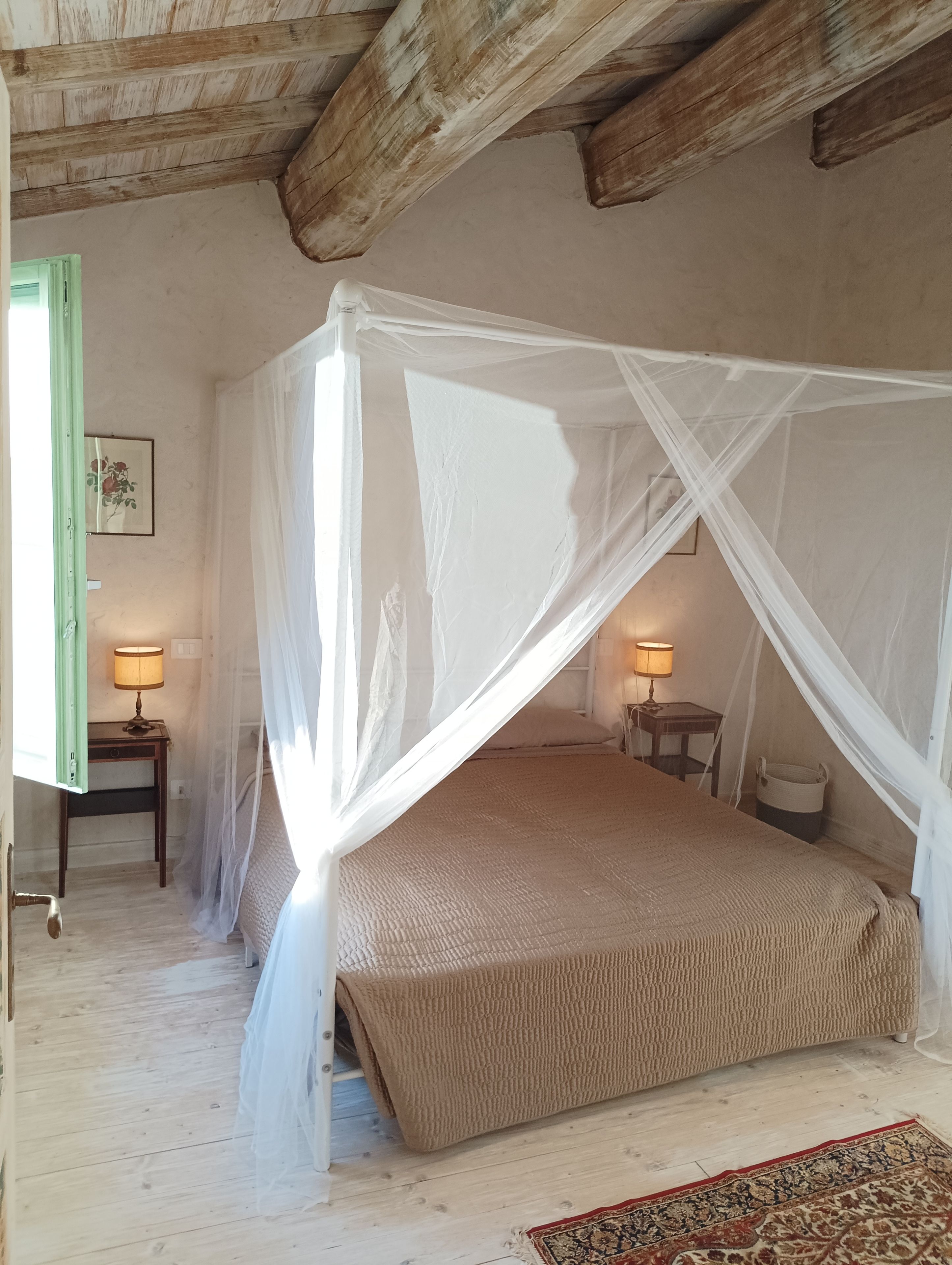 A bedroom with a four-poster bed, a wooden ceiling, and a small bedside table with a lamp.