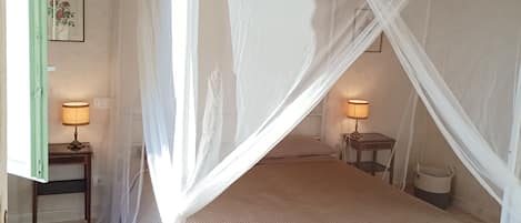 A bedroom with a four-poster bed, a wooden ceiling, and a small bedside table with a lamp.