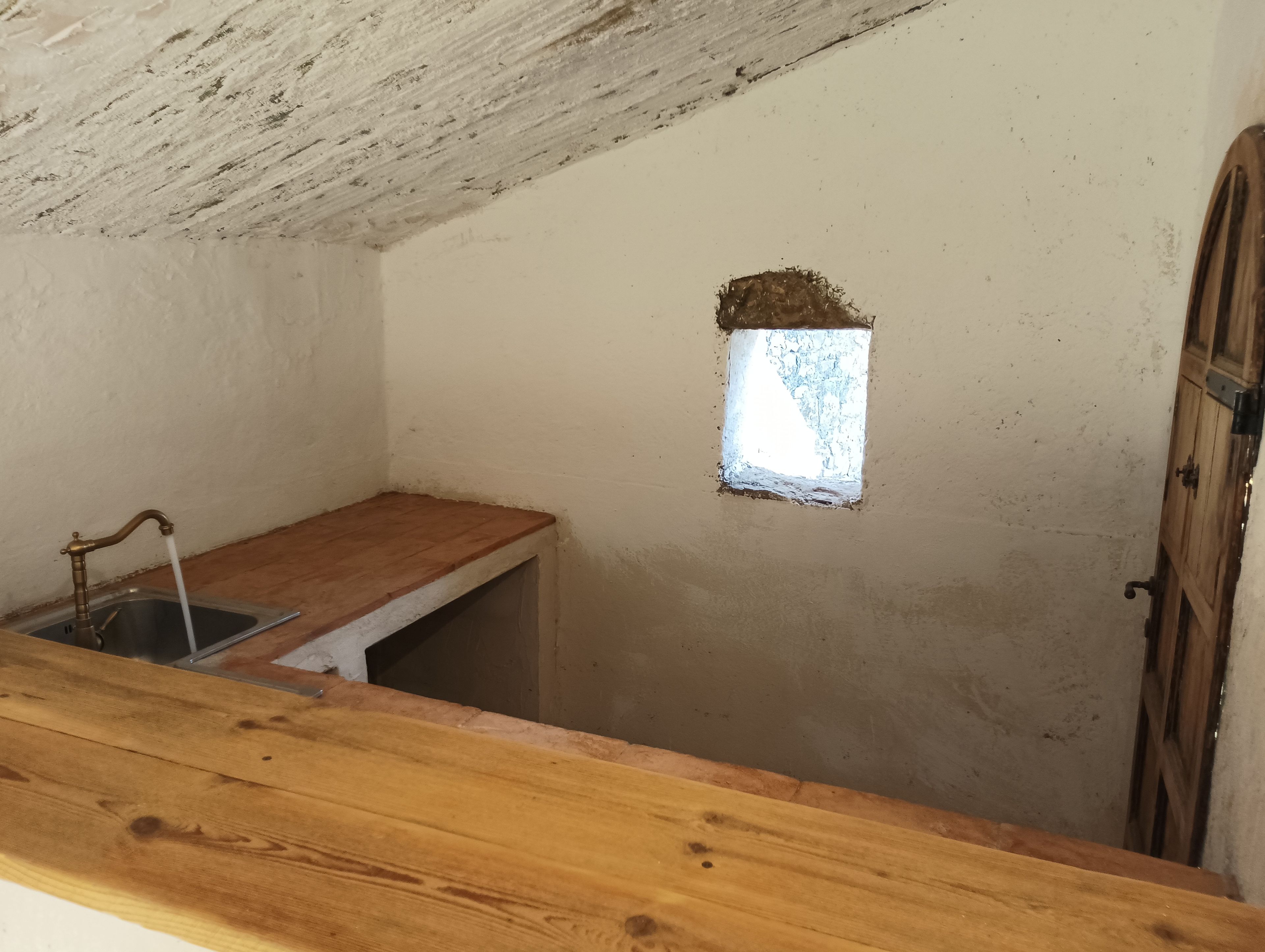 A small kitchen with a wooden countertop, a sink, and a window with a rough exterior.