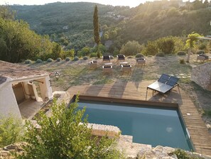 Ein Poolbereich mit Holzterrasse, Liegestühlen und Blick auf eine Hügelkette.