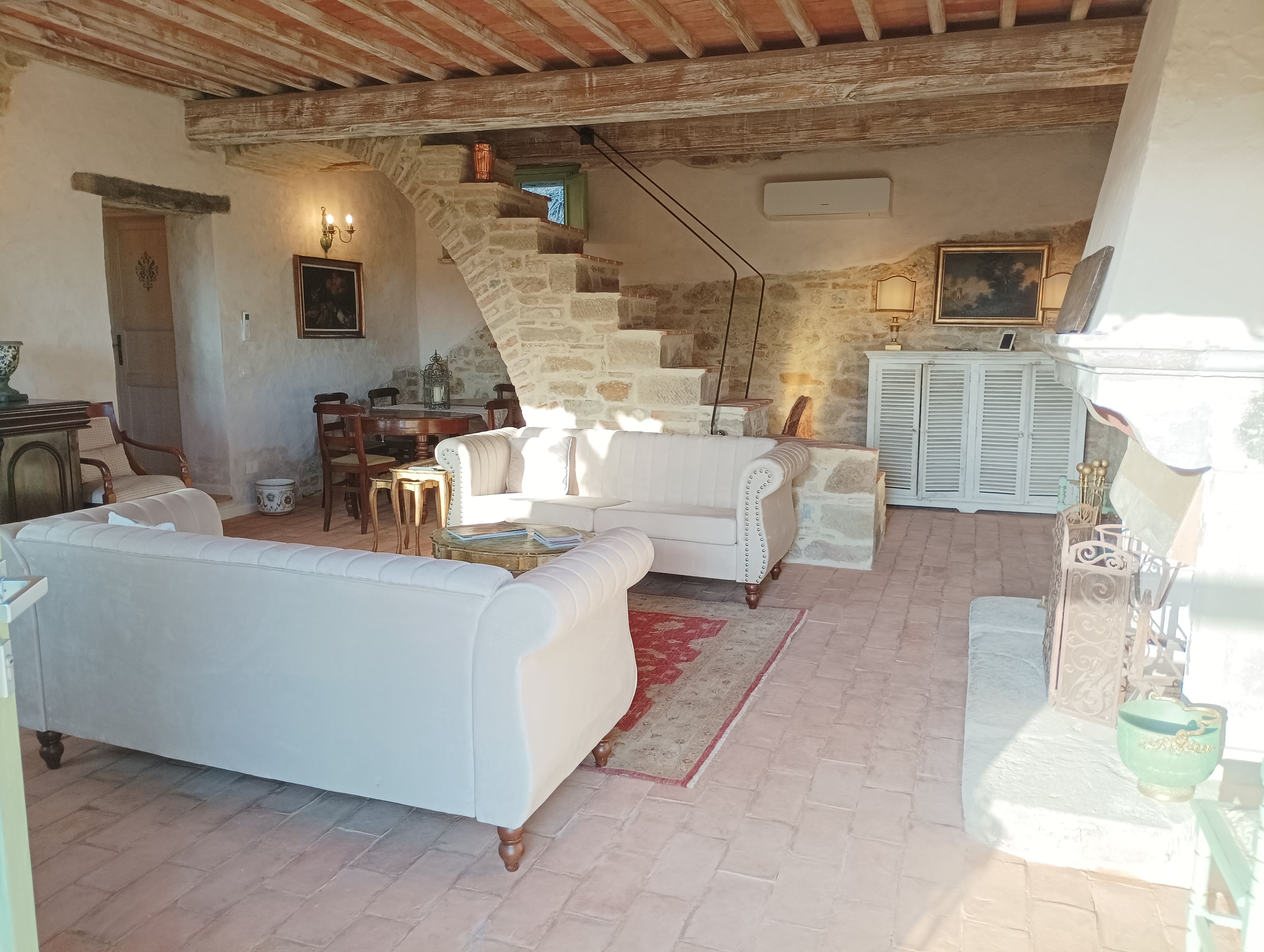 Un intérieur rustique avec un canapé blanc, une table à manger et un escalier menant à un niveau supérieur.
