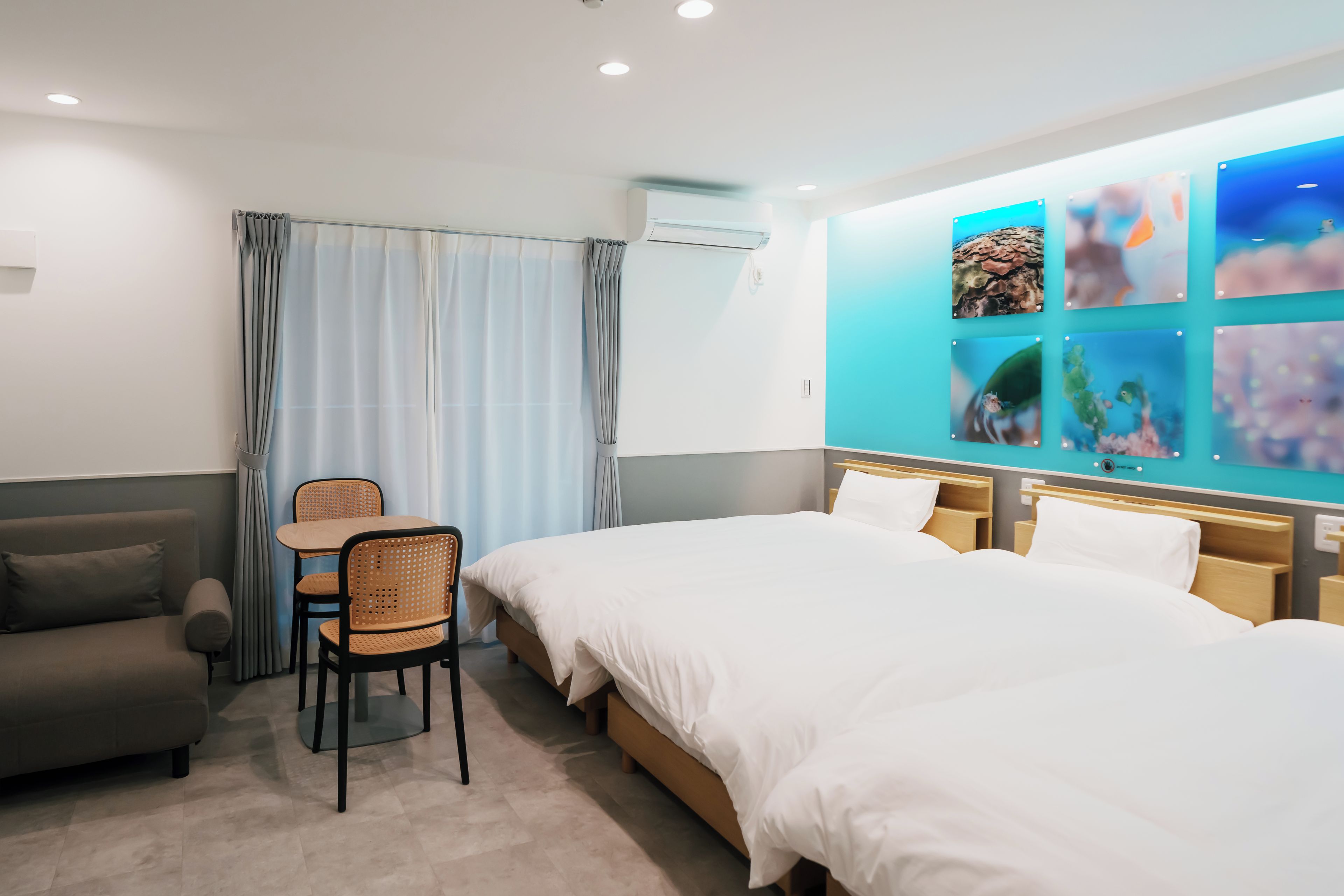 Habitación de hotel con cama, sofá, mesa y una silla. Se ve una ventana decorada con una obra de arte.