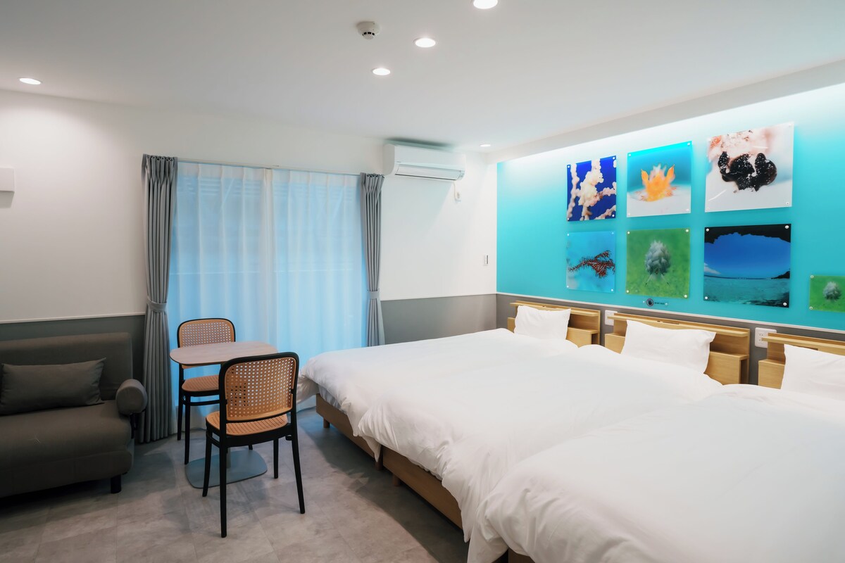 A hotel room with a bed, a desk, a chair, and a sofa. There are ceiling lights and an air conditioning unit.