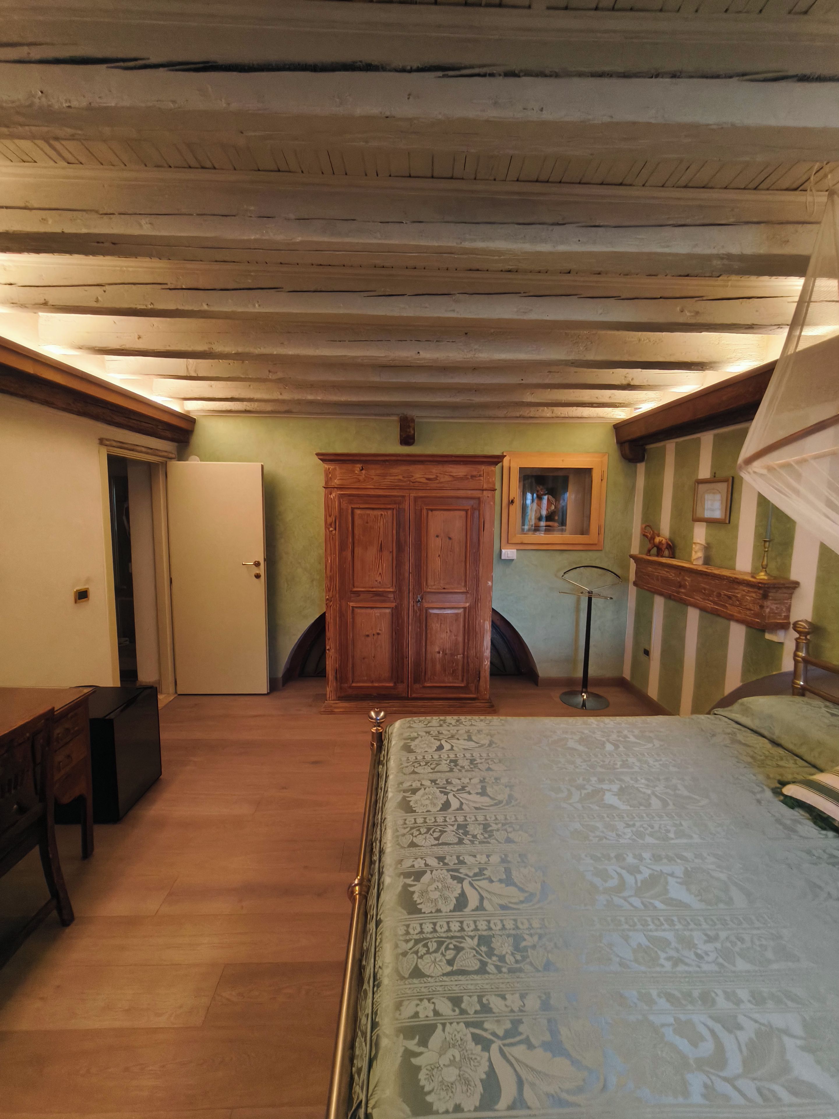 A bedroom with a bed, wooden wardrobe, and a mirror on the wall.