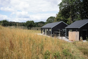 A modern building with a flat roof and large windows, surrounded by tall grass and trees. - Natural plot with a view of Mols Bjerge (Ebeltoft)