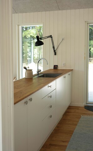 A kitchen with a wooden countertop, white cabinets, a black pendant light, and a window with a view of trees. - Natural plot with a view of Mols Bjerge (Ebeltoft)