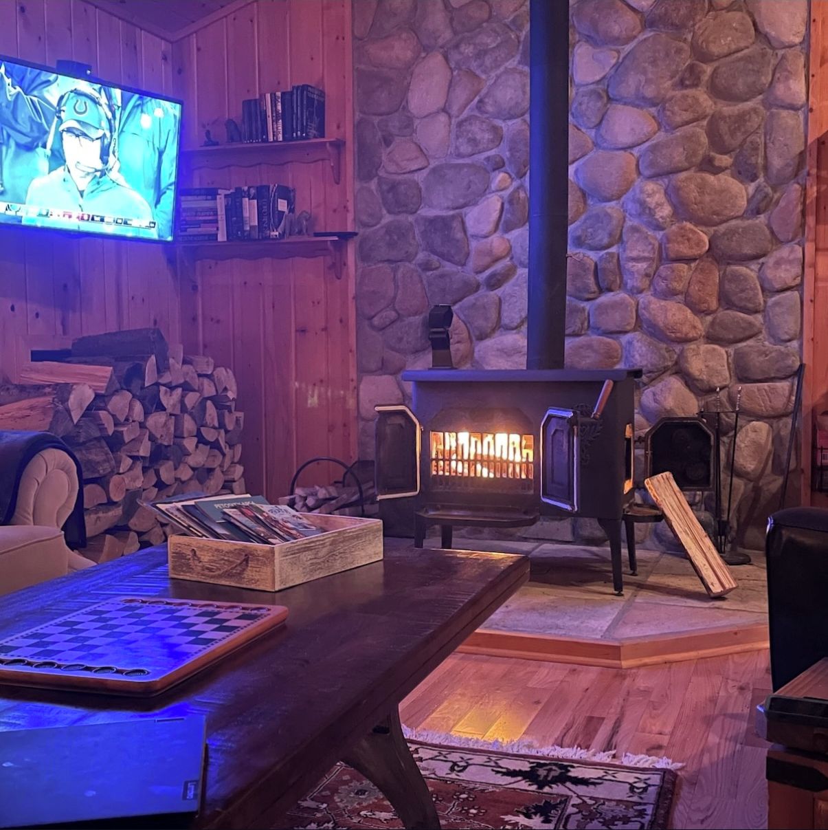 A cozy room with a stone wall, a fireplace, a television, and a chessboard.
