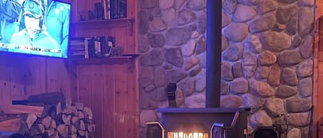 A cozy room with a stone wall, a fireplace, a television, and a chessboard.