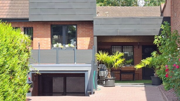 Een tweelaags gebouw met een garage, een balkon met plantenbakken en een patio met tuinmeubilair.