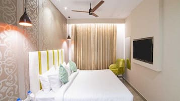A hotel room with a bed, a TV mounted on the wall, a ceiling fan, and a window with curtains.