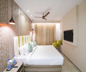 A hotel room with a bed, a TV mounted on the wall, a ceiling fan, and a window with curtains.
