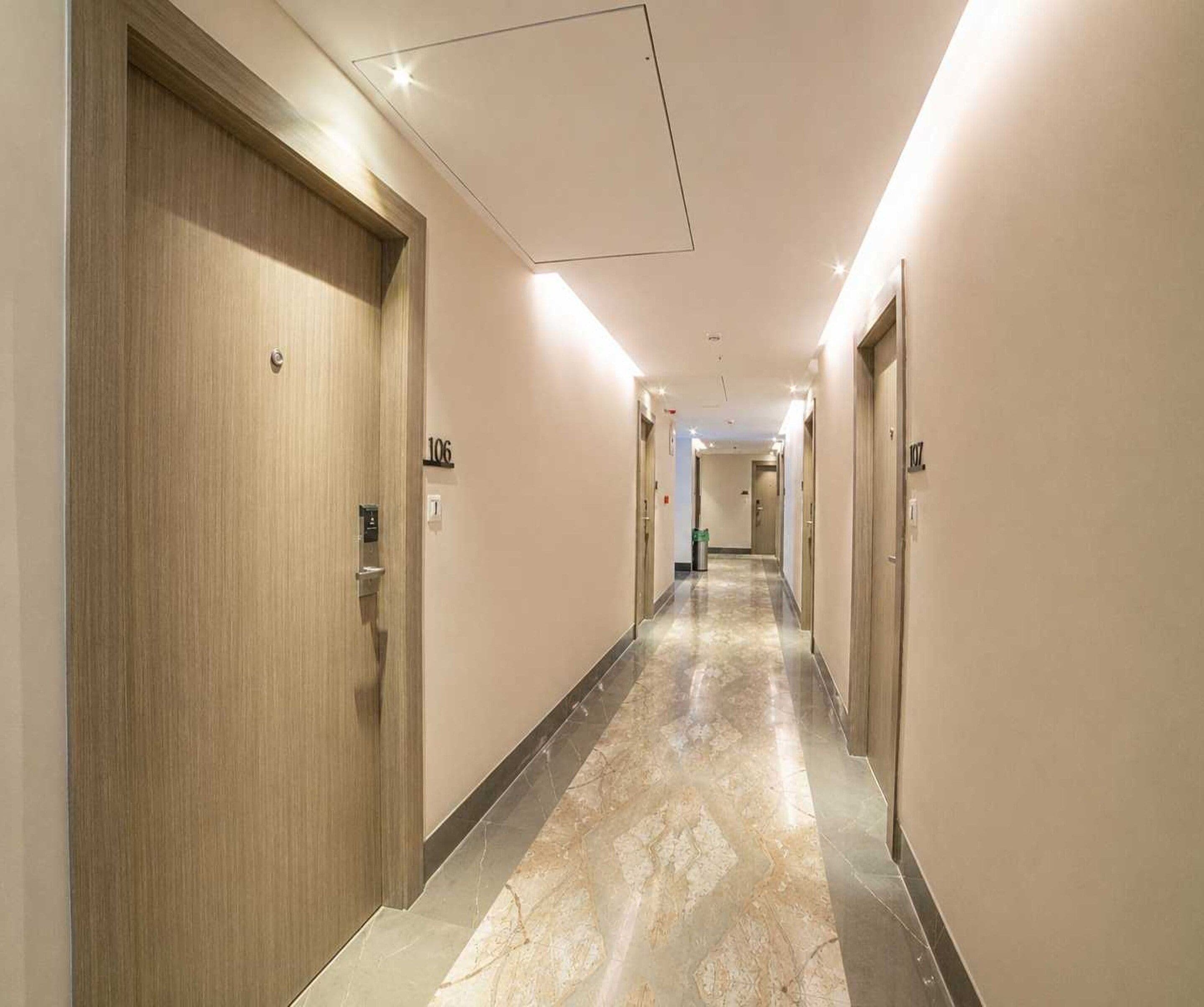 Een hotelgang met deuren met de nummers 106 en 107, een marmeren vloer en een plafond met inbouwverlichting.