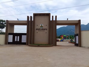 Una entrada con portón a Araku Aranya Resort, con cielo despejado y montañas al fondo.