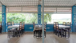 A covered outdoor dining area with tables and chairs, a decorative ceiling, and a view of greenery. - Classic Padmavati Lake Resort (Chittorgarh)