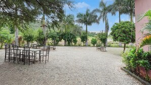 An outdoor seating area with tables and chairs, surrounded by trees and a gravel ground. - Classic Padmavati Lake Resort (Chittorgarh)