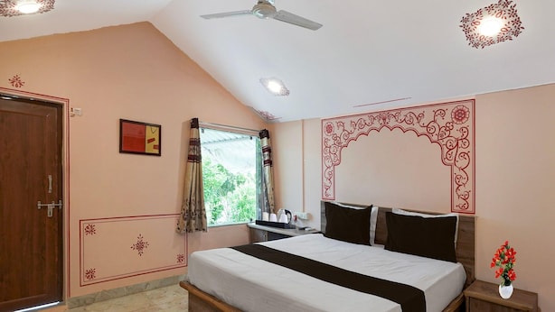 A bedroom with a bed, a ceiling fan, a window with curtains, and a decorative wall design. - Classic Padmavati Lake Resort (Chittorgarh)