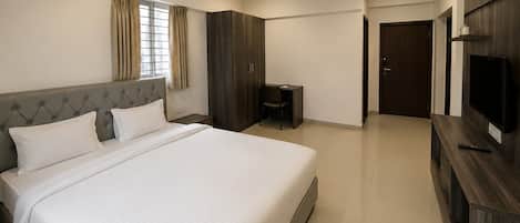 A hotel room with a large bed, a desk, a chair, a wardrobe, a television, and a ceiling fan.