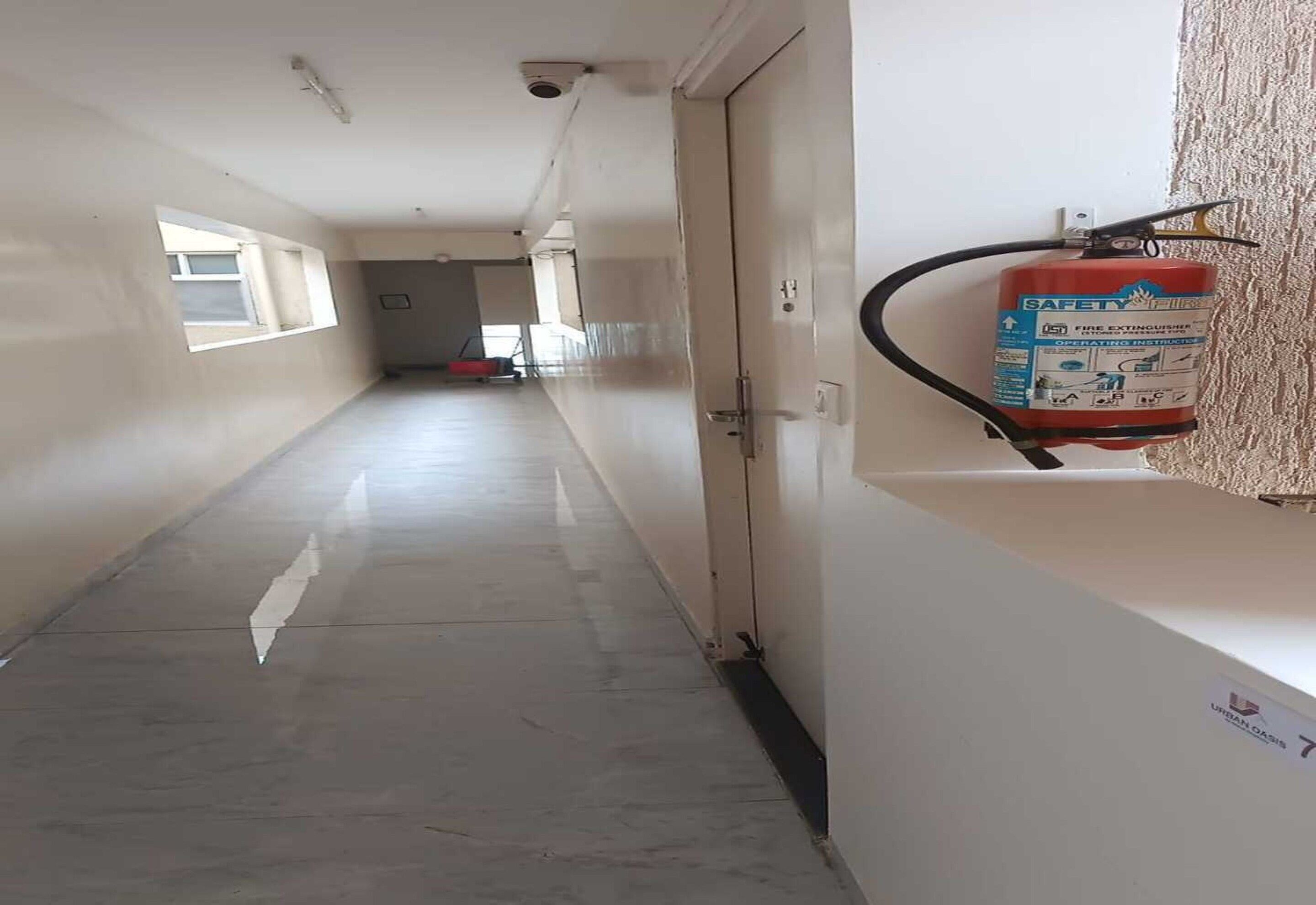 Un pasillo con un extintor en la pared, una puerta al final y una ventana a la izquierda.