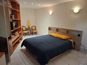 Um quarto com cama, escrivaninha, duas cadeiras e estante.