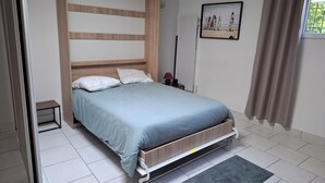 A bedroom with a bed, a bedside table, a nightstand, a wall-mounted lamp, a framed picture, and a window with curtains. - Vrbo Property (Seclin)