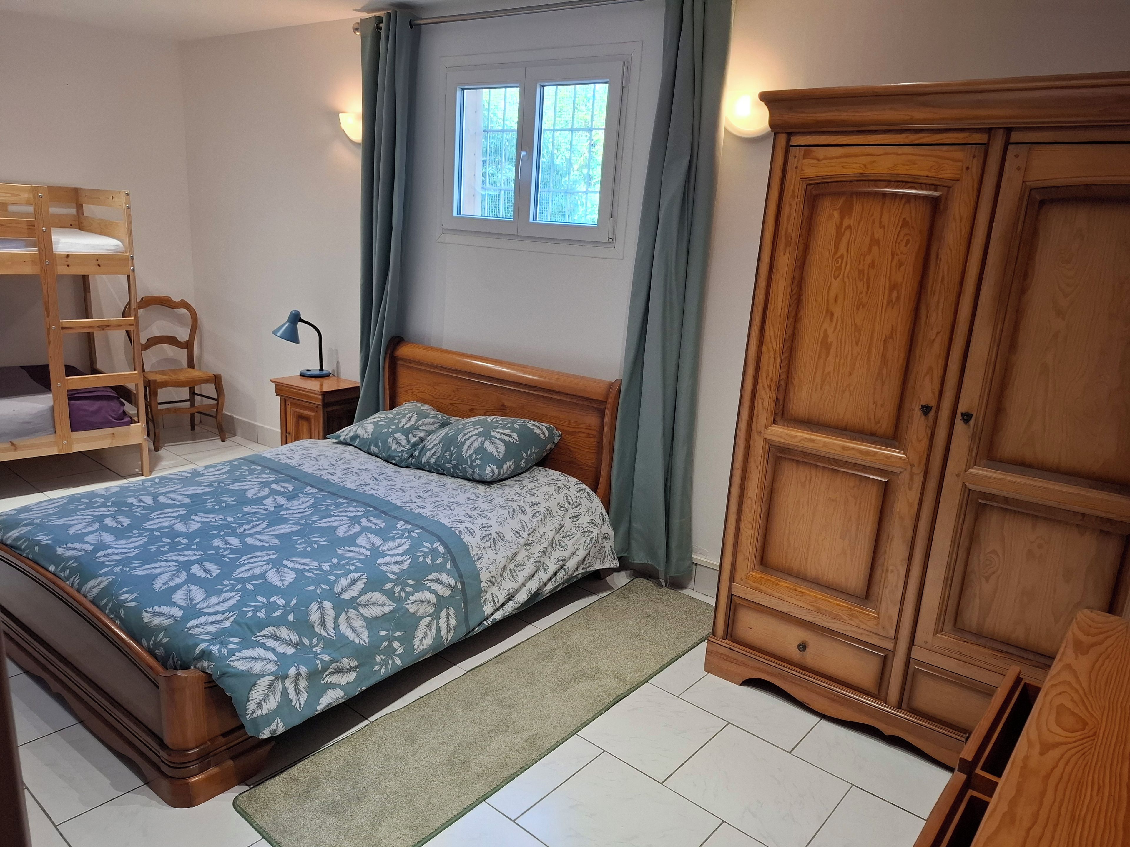 Un dormitorio con una cama de madera, una mesita de noche, una silla, un armario y una ventana con cortinas.