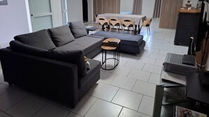 A modern living room with a dark grey sofa, a small coffee table, and a dining area with a table and chairs. - Vrbo Property (Seclin)