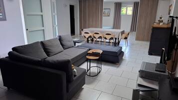 Een moderne woonkamer met een donkergrijze bank, een klein bijzettafeltje en een eethoek met een tafel en stoelen.