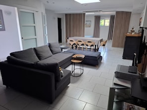 Uma sala de estar moderna com um sofá cinza escuro, uma pequena mesa de centro e uma área de jantar com uma mesa e cadeiras.