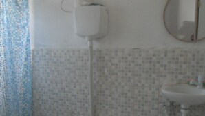 Casa de banho com sanita, lavatório, espelho e chuveiro.