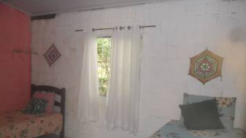 A room with two beds, a window with curtains, and a wall with a geometric decoration.