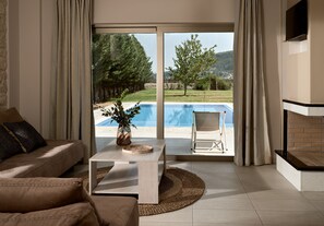 Una sala de estar con un sofá, una mesa de centro con un florero y vistas a una piscina y paisajes al aire libre.