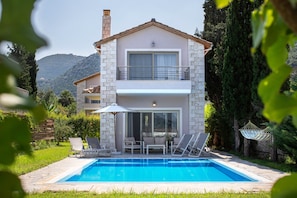 Una casa de dos pisos con piscina, mobiliario exterior y vistas del paisaje circundante.