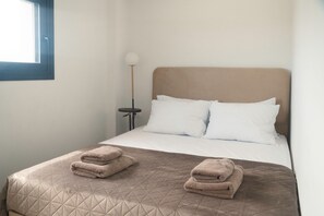 Ein Einzelbett mit gestepptem Kopfteil, zwei Kissen und zwei gefaltete Handtücher am Fußende.