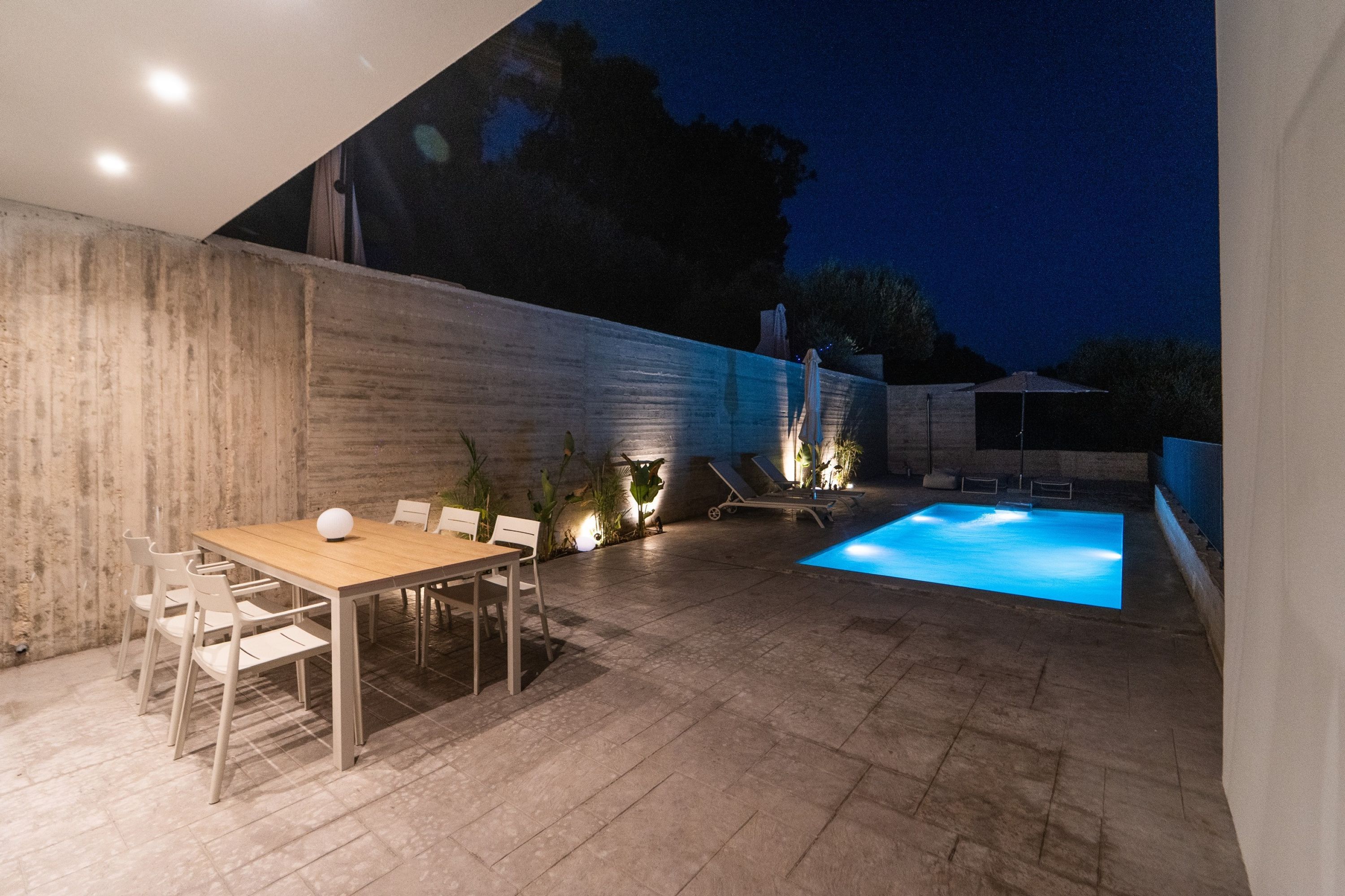 An outdoor patio area with a pool, a dining table with chairs, and lounge chairs.