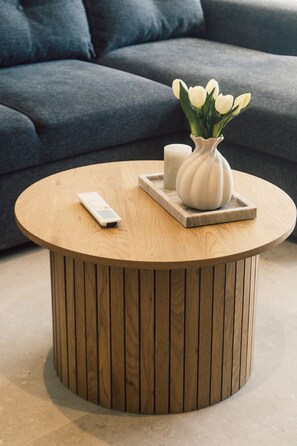 Ein runder Couchtisch aus Holz mit einer Fernbedienung und einer Blumenvase darauf.