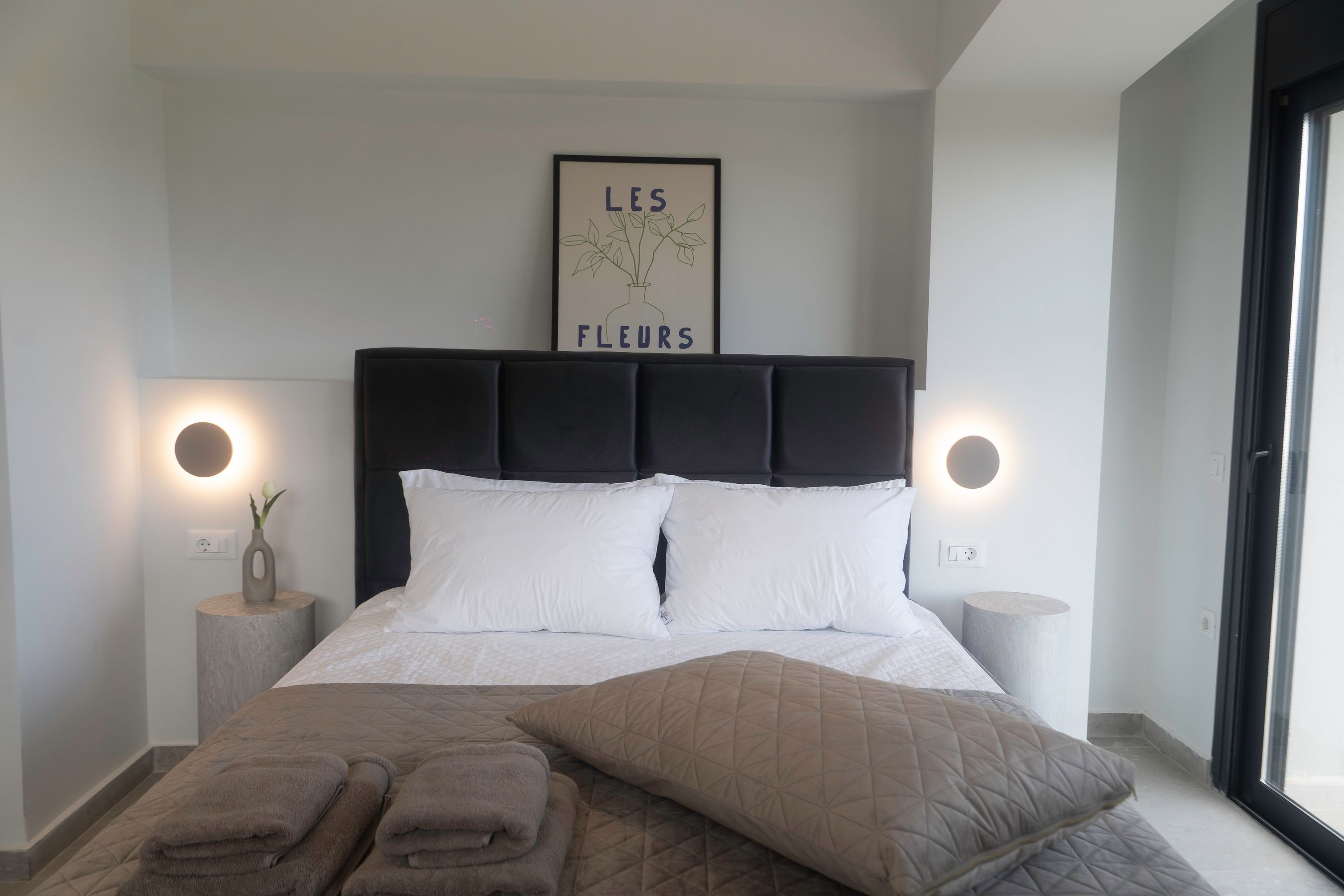 Une chambre moderne avec un grand lit, deux tables de chevet, une tête de lit dotée d’un éclairage intégré et une œuvre d’art accrochée au mur.
