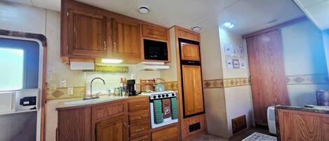 A compact kitchen with wooden cabinets, a microwave, a stove, and a sink.